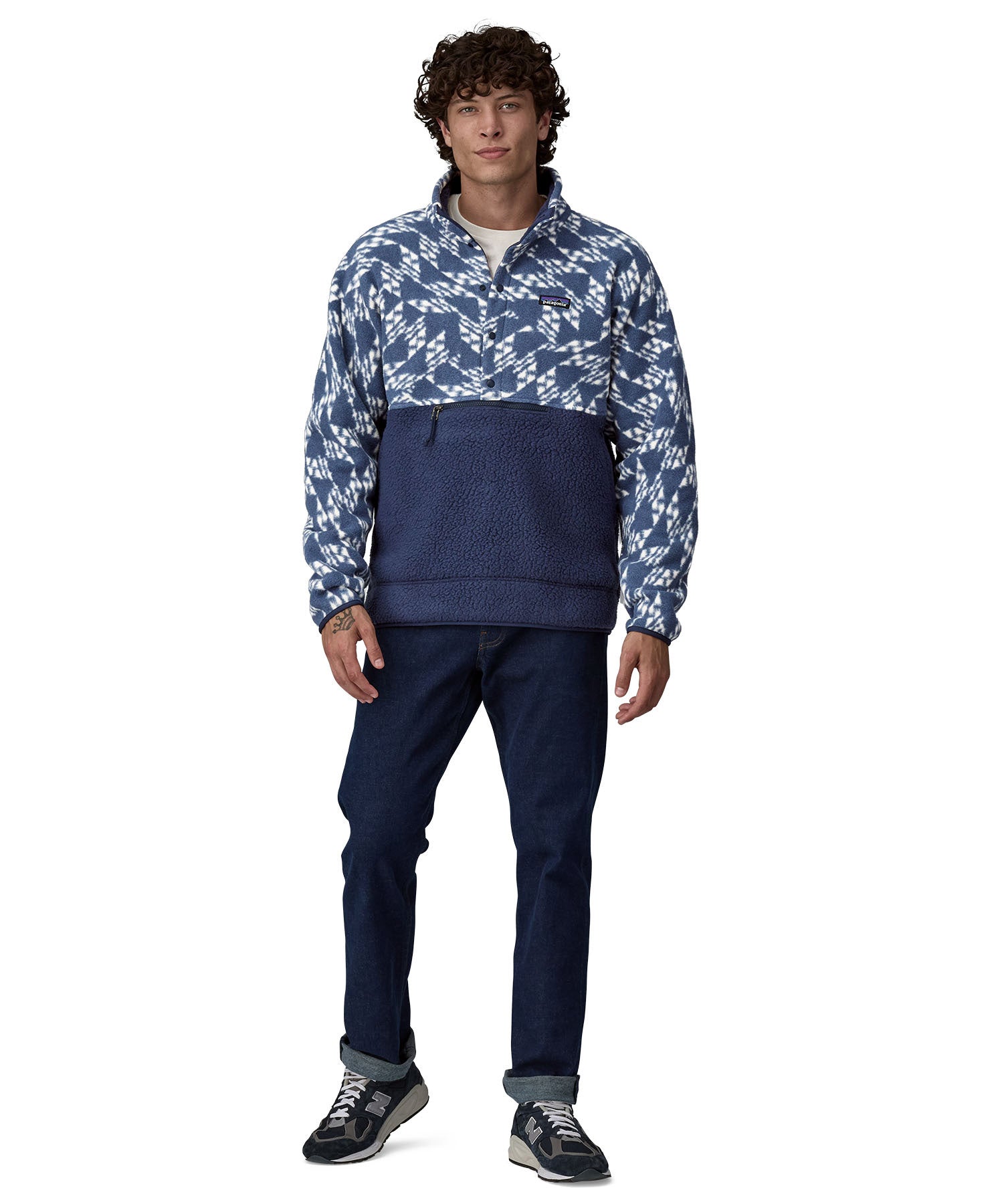 A man wearing a Patagonia Men's Retro Pile 1/2 Snap Pull Over in a New Navy design stood in front of a plain background. He is also wearing dark denim jeans and black coloured trainers. 
