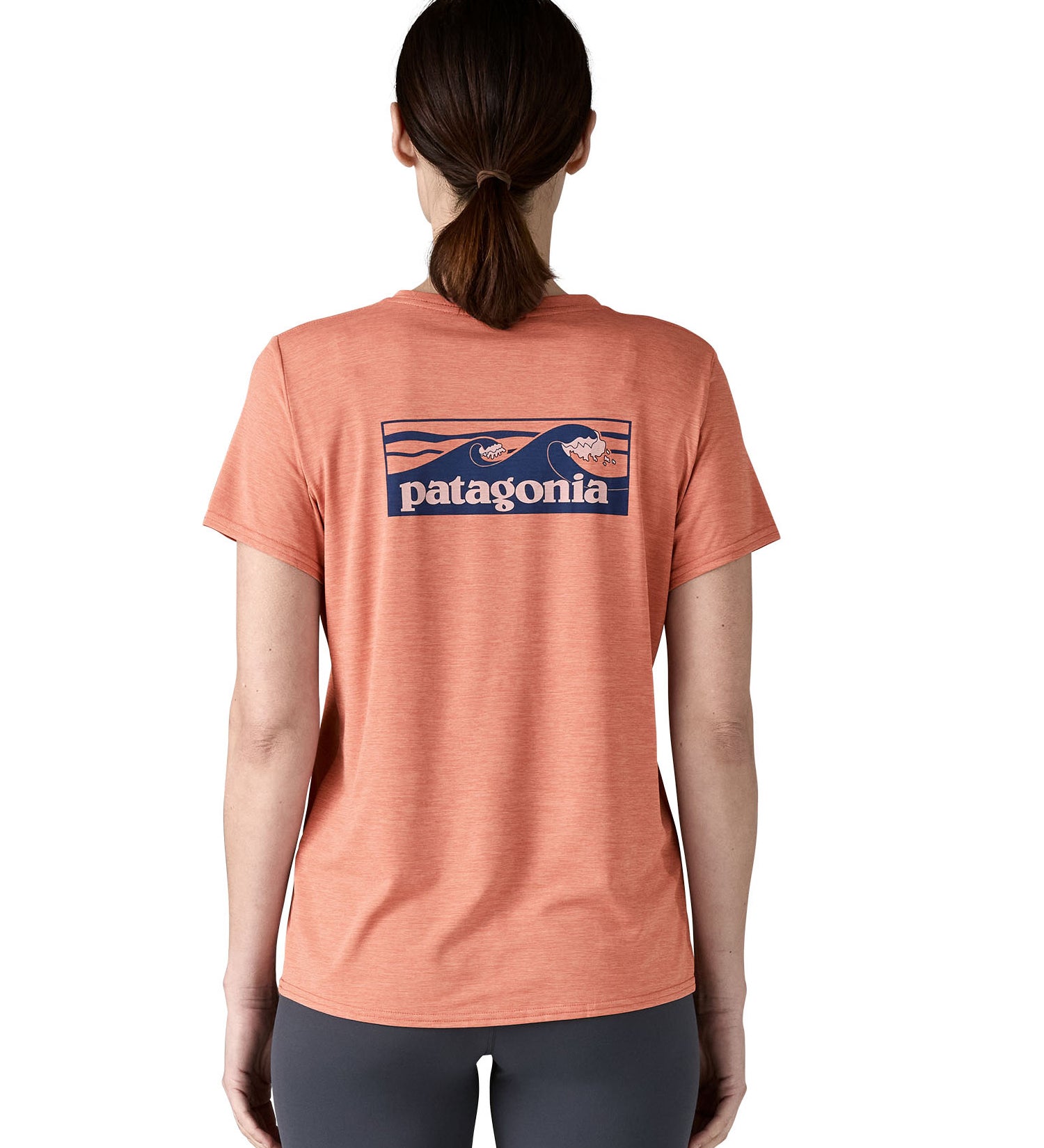 Tha back of the Patagonia Women's Capilene Cool Daily Graphic Shirt worn by an adult showing the short sleeved pastel pink top with wave graphic printed across the back