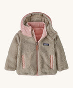Patagonia little kids tribbles hoody. A reversible coat showing the natural fleece alternative side. Features a logo patch on the chest and 2 side pockets with popper fastenings