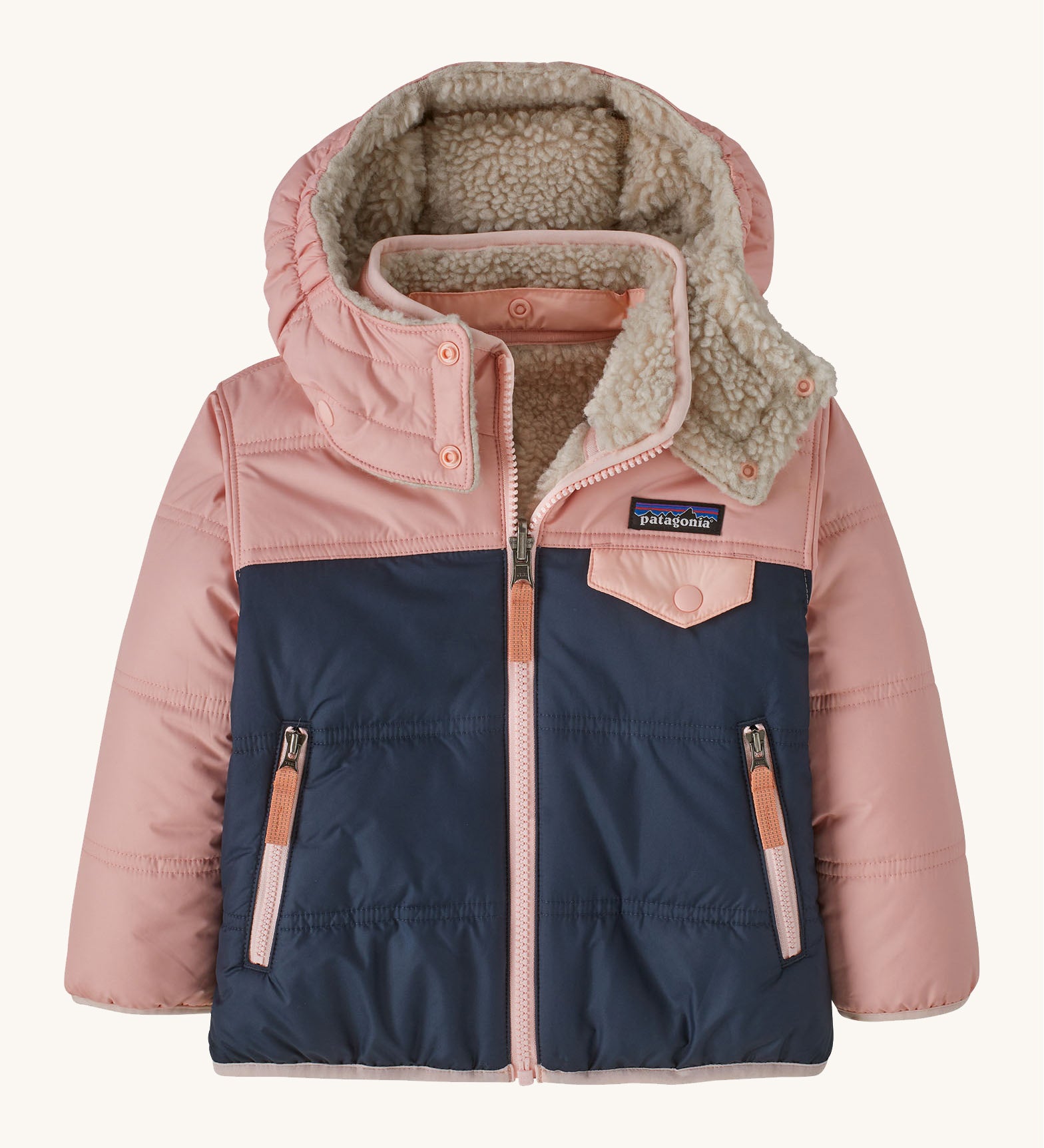 Patagonia little kids tribbles hoody. A reversible coat showing a pink and navy hooded coat and natural fleece inner for warmth. Features a small chest pocket with popper fastening and 2 side zip pockets