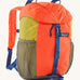 The Patagonia Kids Refugito 12L Backpack   , a vibrant orange backpack with block mustard colour side panels. Features 2 side mesh pockets in grey and a blue buckle to close the lid. Logo patch is stitched on the front panel.