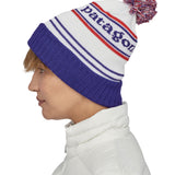 Side view of the Patagonia park stripe viking blue. Worn by an adult it features a red, white and blue pom pom pom and blue turn up ribbed brim with the logo stitched into the hat