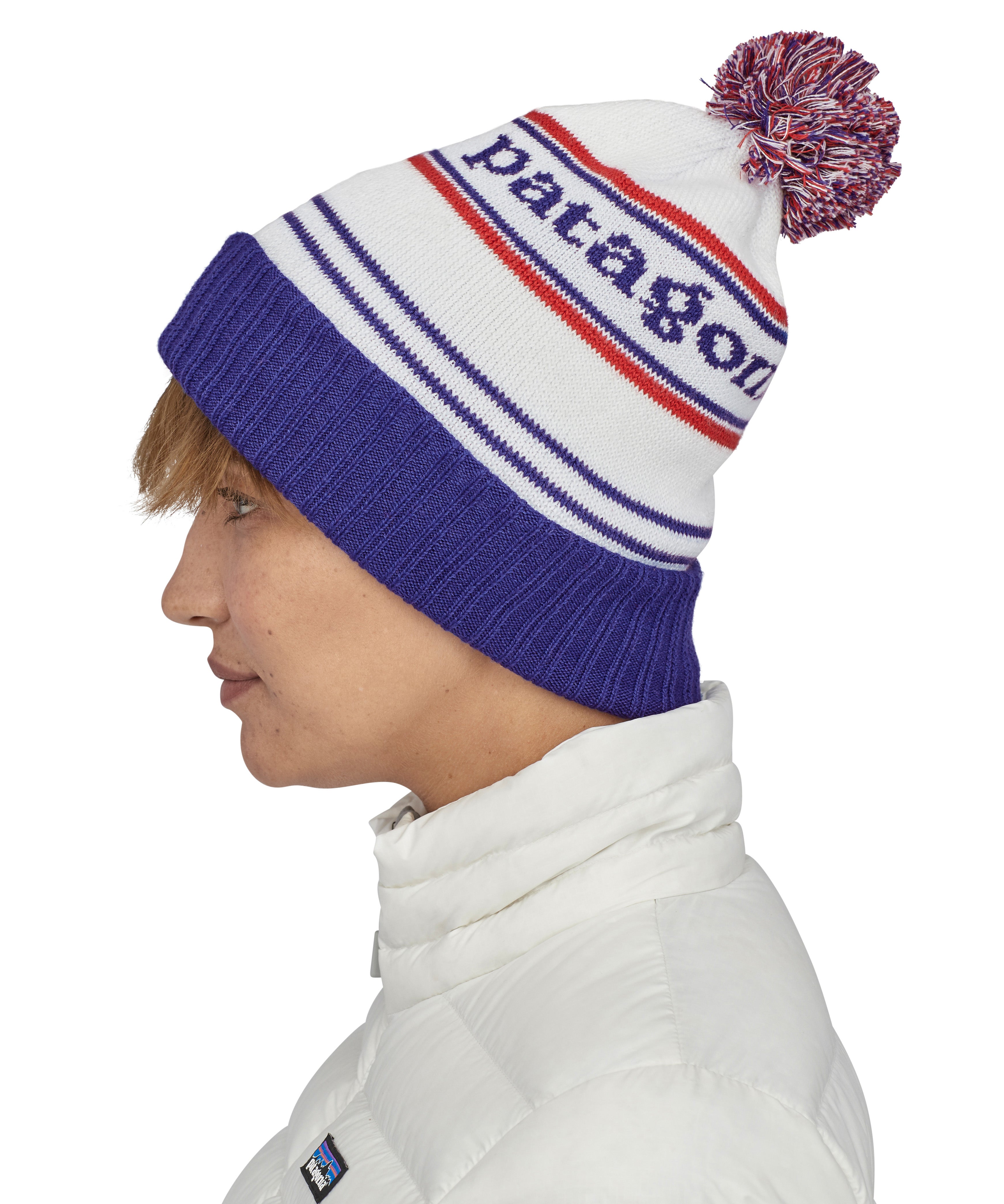 Side view of the Patagonia park stripe viking blue. Worn by an adult it features a red, white and blue pom pom pom and blue turn up ribbed brim with the logo stitched into the hat