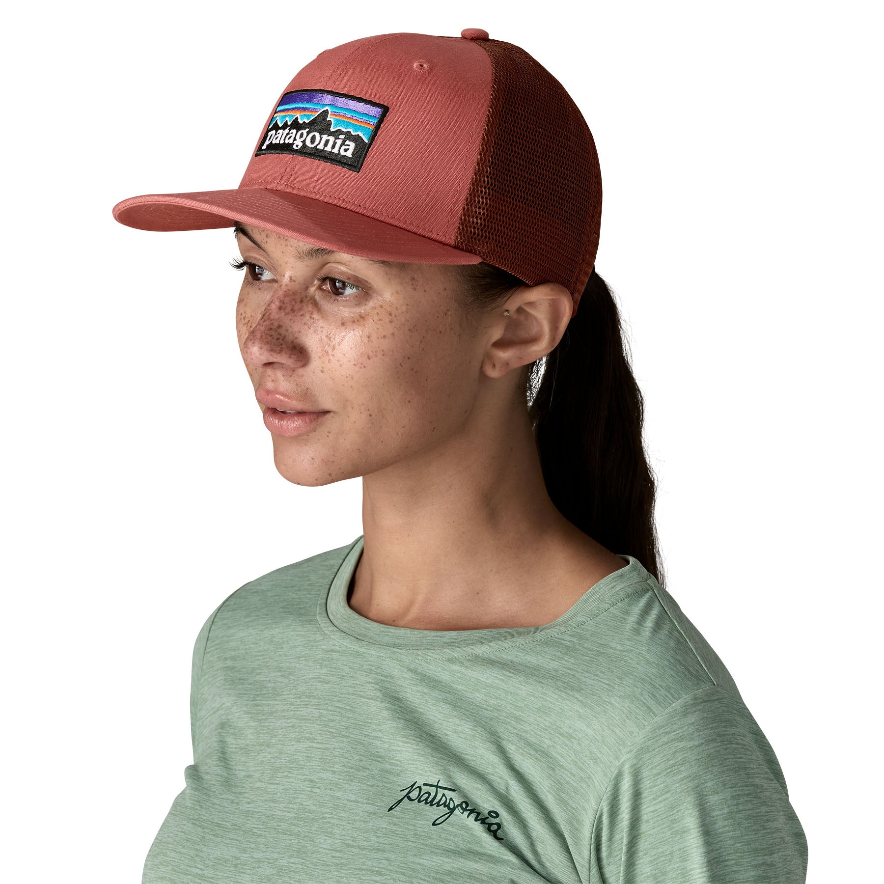 A woman wearing the Patagonia adult red potters hat. A trucker style cap with a mesh back and logo embroidery on the front panel available at Babipur.
