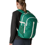 Back of woman wearing the Patagonia's 26L refugio backpack in green with cream straps and top handle.