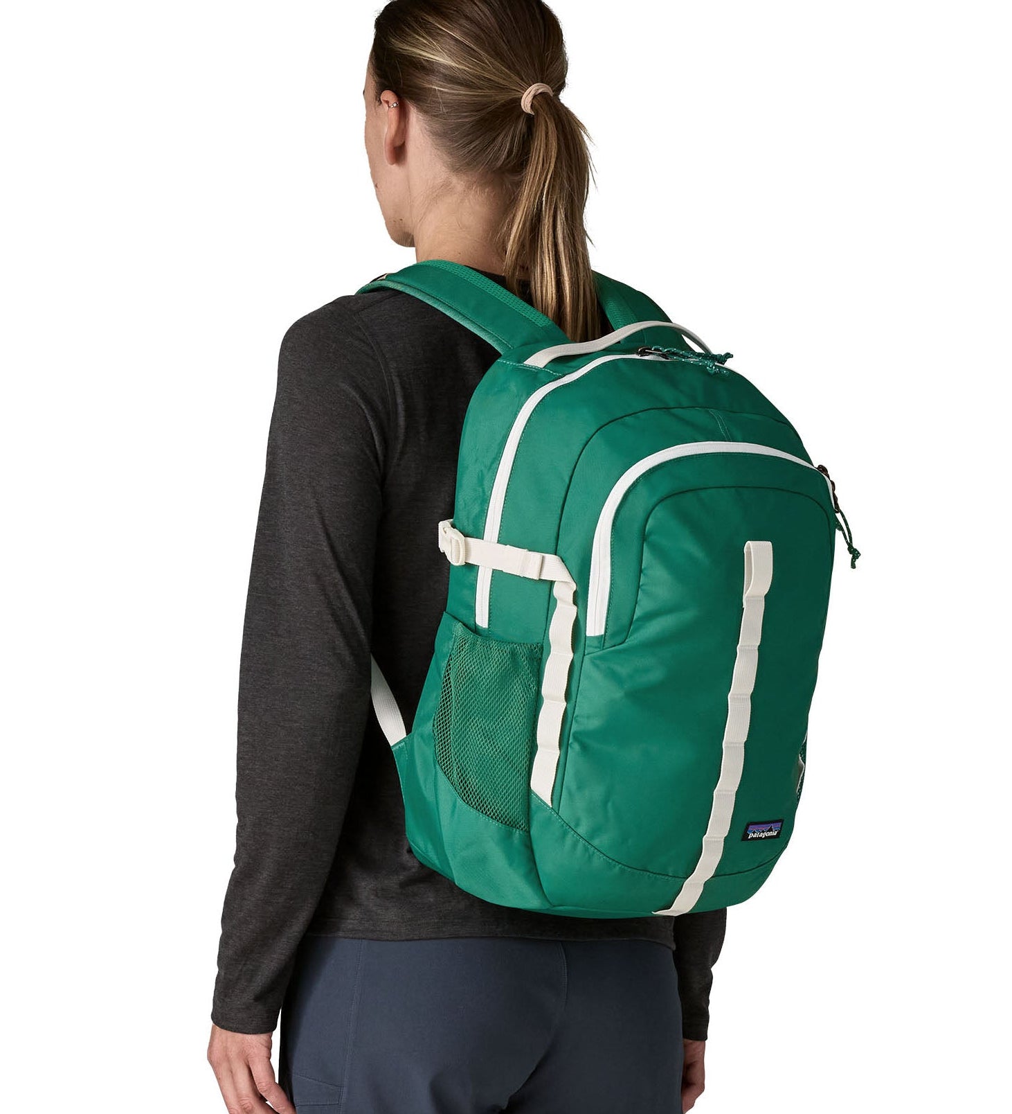 Back of woman wearing the Patagonia's 26L refugio backpack in green with cream straps and top handle.