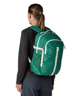 Back of woman wearing the Patagonia's 26L refugio backpack in green with cream straps and top handle.