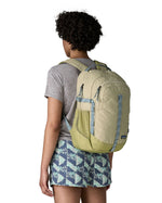 Person wearing the Patagonia 26L refugio backpack in stone with grey straps and top handle.