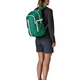 Woman wearing the Patagonia 26L refugio backpack in green with cream straps and top handle.