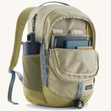Patagonia refugio backpack in stone with open front compartment with stationery placed inside and a bottle in the side holder.