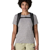 Woman wearing the Patagonia's 26L refugio backpack in black with matching chest strap and quick release buckle.