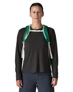 Woman wearing the Patagonia's 26L refugio backpack in green with cream chest strap and quick release buckle.