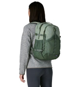 Woman wearing the Patagonia refugio day pack 30L backpack in cover green on her back.