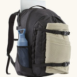 Patagonia refugio day pack 32 litre backpack in black with laptop in sleeve at back, blanket in the equipment straps at the front and a bottle in the holder on the side. 