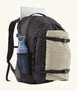 Patagonia refugio day pack 32 litre backpack in black with laptop in sleeve at back, blanket in the equipment straps at the front and a bottle in the holder on the side. 