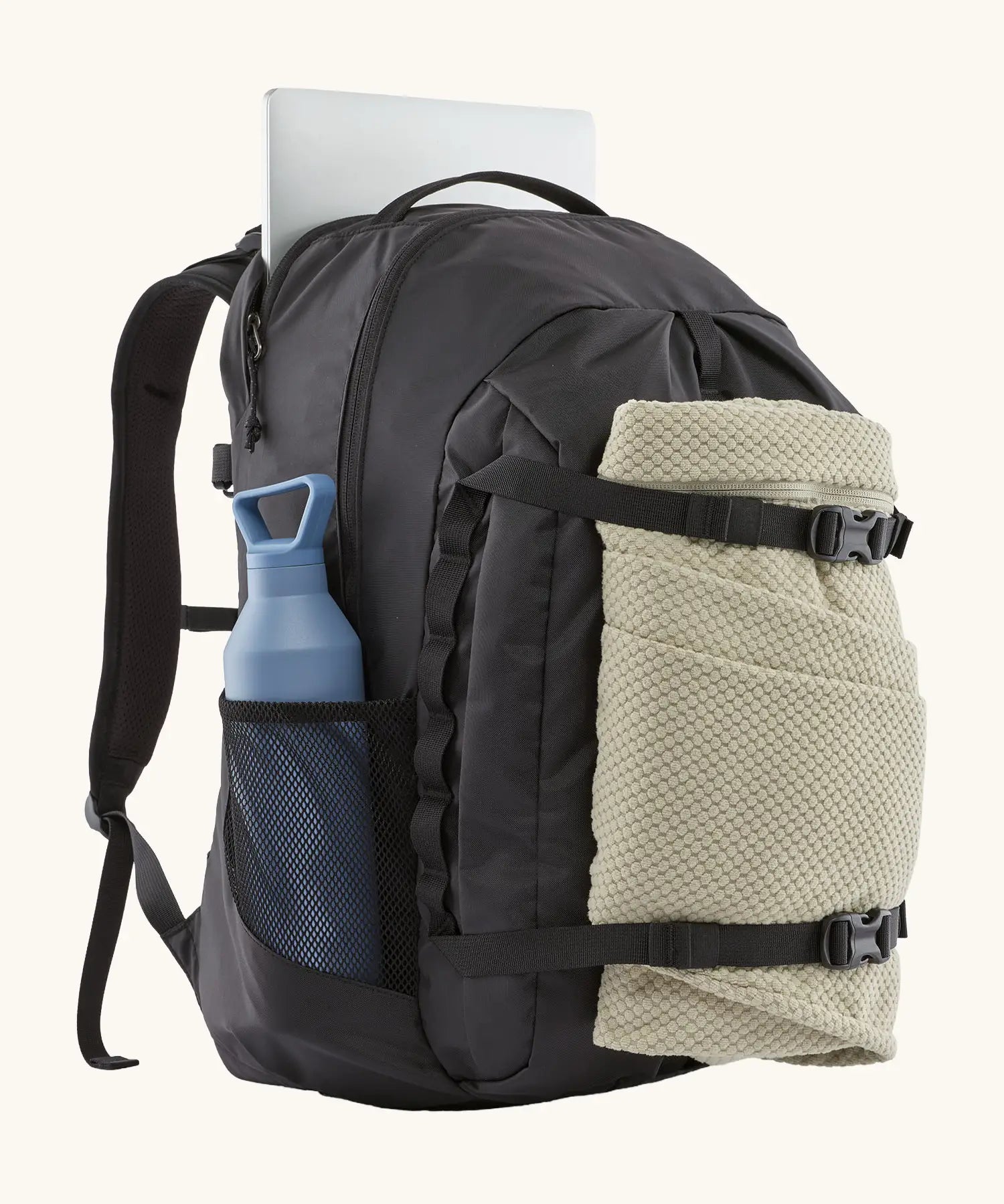 Patagonia refugio day pack 32 litre backpack in black with laptop in sleeve at back, blanket in the equipment straps at the front and a bottle in the holder on the side. 