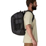 Side view of a man wearing a Patagonia refugio day pack 32 litre backpack in black on his back. 