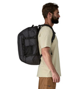 Side view of a man wearing a Patagonia refugio day pack 32 litre backpack in black on his back. 