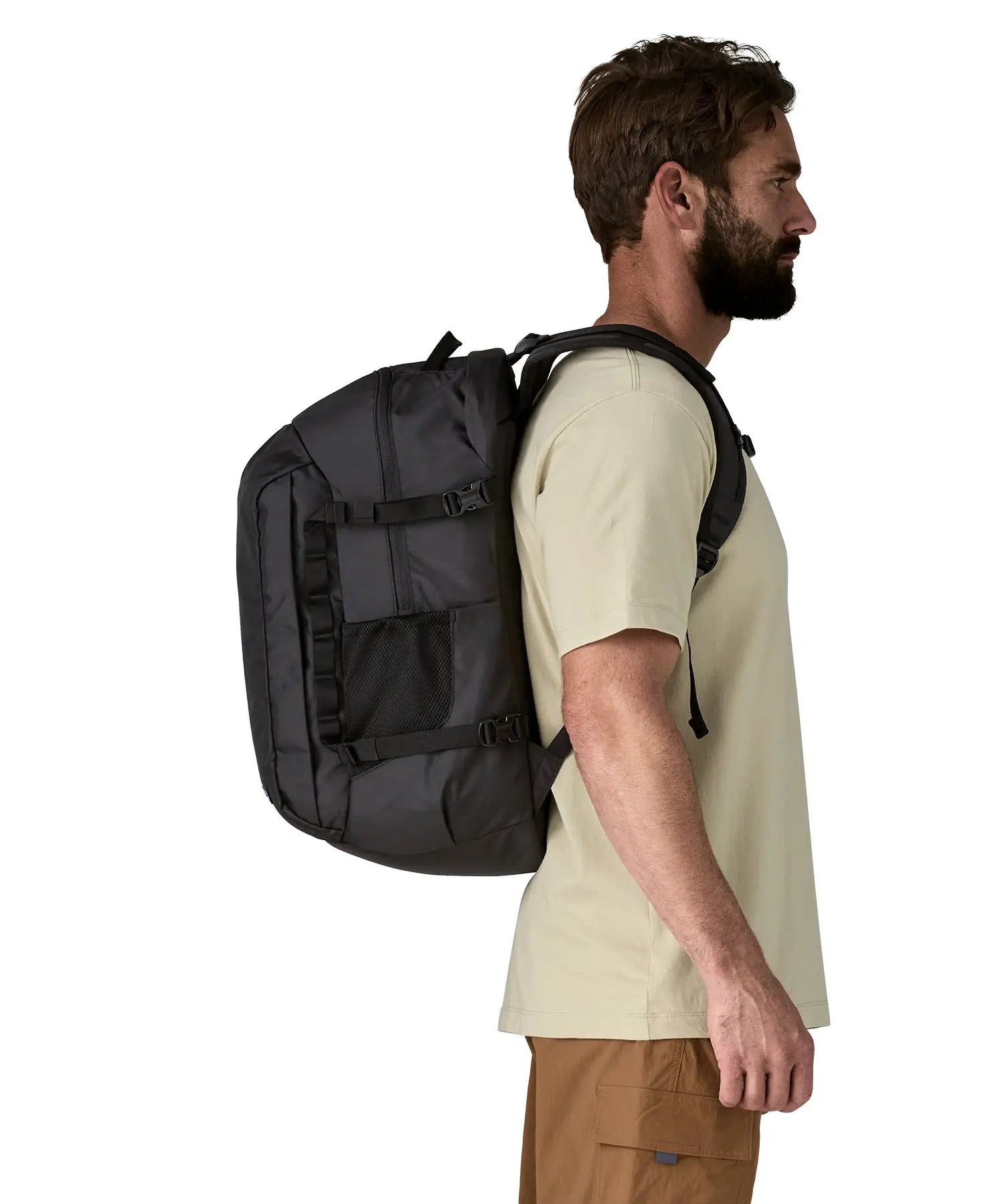 Side view of a man wearing a Patagonia refugio day pack 32 litre backpack in black on his back. 