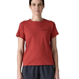 A woman wearing the Patagonia sequoia red short sleeve shirt showing the brand name printed in black on the chest. 