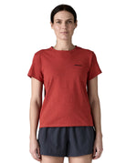 A woman wearing the Patagonia sequoia red short sleeve shirt showing the brand name printed in black on the chest. 