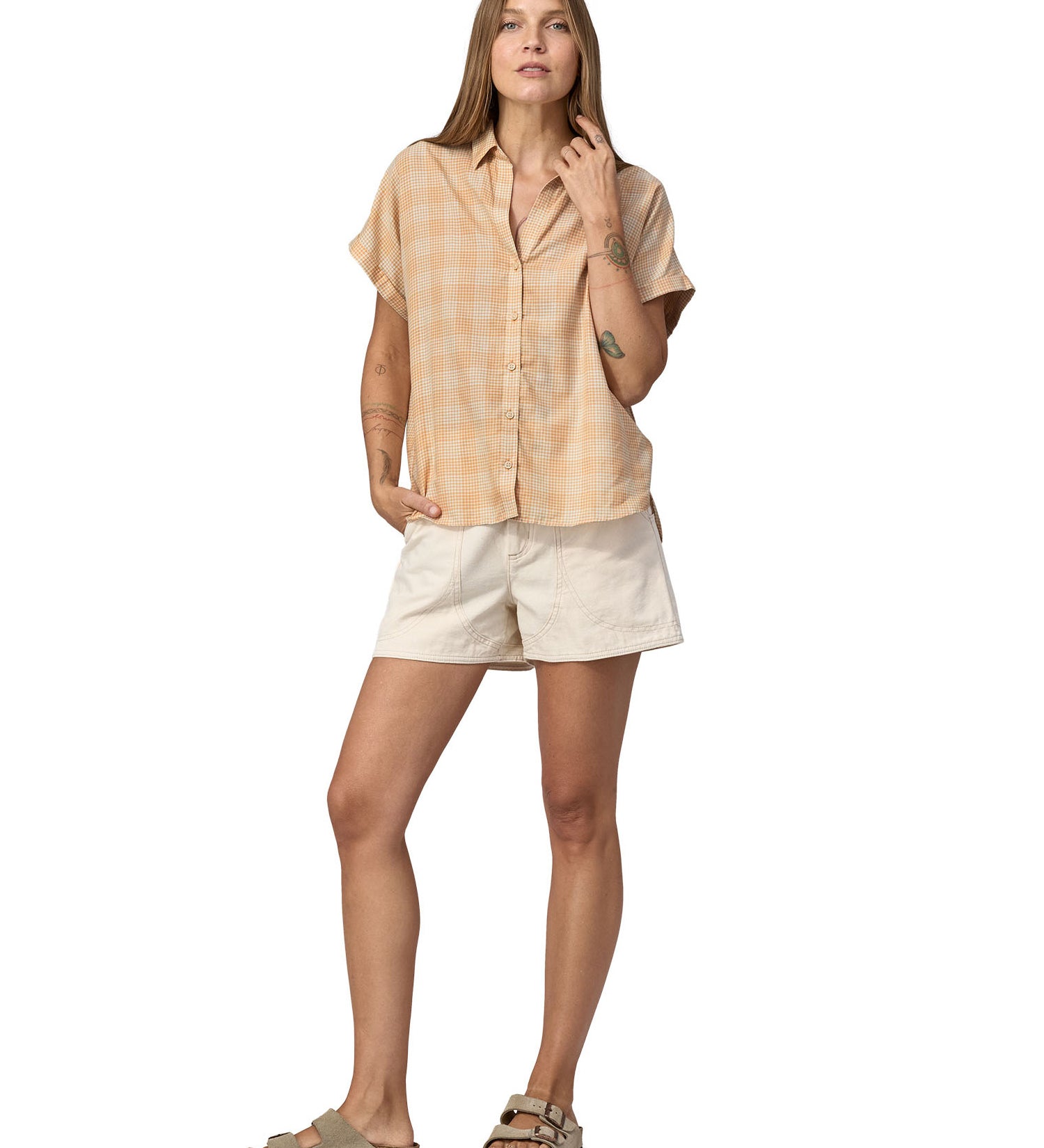Women wearing a Patagonia Women's A/C Shirt in a pale golden yellow and white check, made from a blend of organic cotton and hemp. She is also wearing white shorts and Birkenstock sandals. 