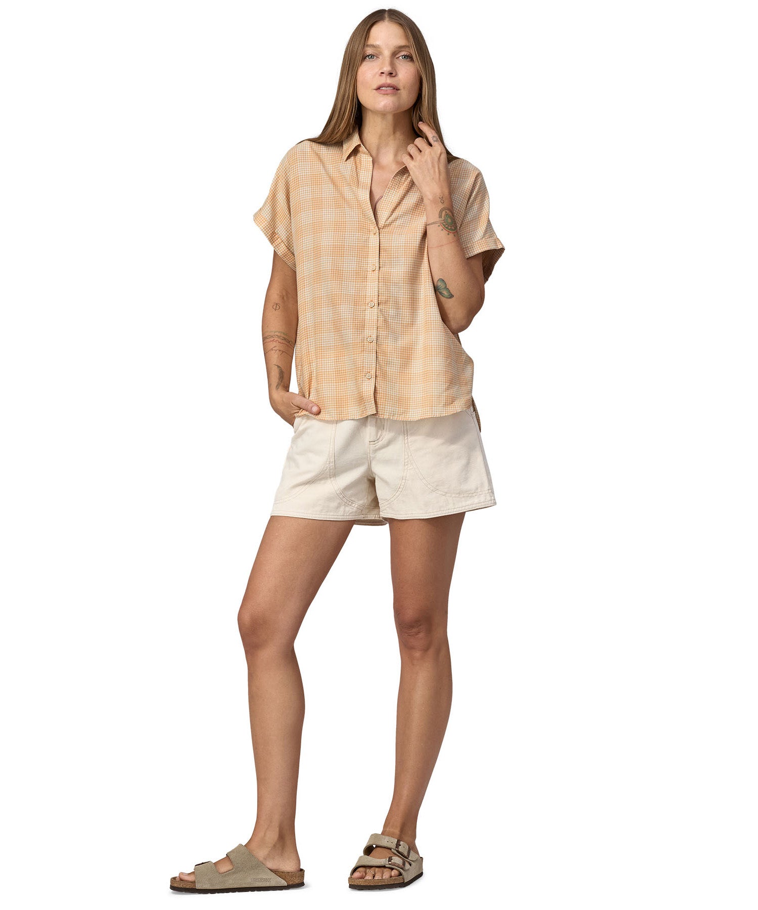 Women wearing a Patagonia Women's A/C Shirt in a pale golden yellow and white check, made from a blend of organic cotton and hemp. She is also wearing white shorts and Birkenstock sandals. 