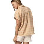 Back of woman wearing white shorts and a Patagonia Women's A/C Shirt in a pale golden yellow and white check, made from a blend of organic cotton and hemp. 