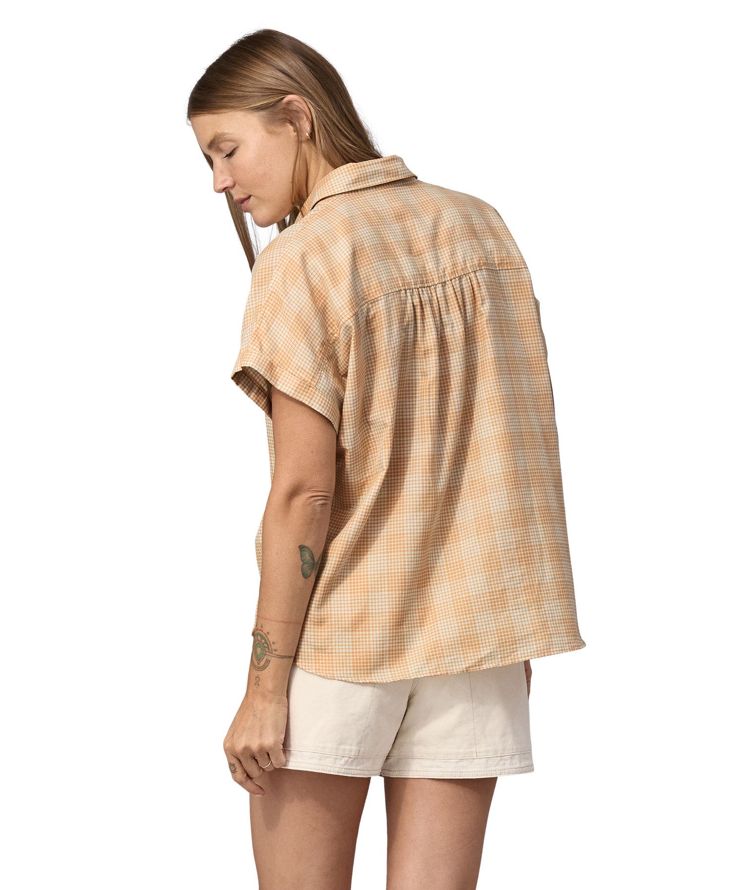 Back of woman wearing white shorts and a Patagonia Women's A/C Shirt in a pale golden yellow and white check, made from a blend of organic cotton and hemp. 