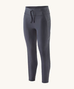 A pair of smolder blue Patagonia running 7/8 tights on a cream background.