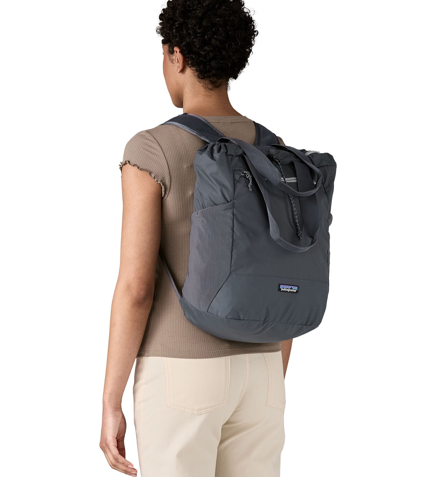 Woman wearing Patagonia's Terravia tote bag in blue worn on the back. Showing carrying handles and mesh side pockets
