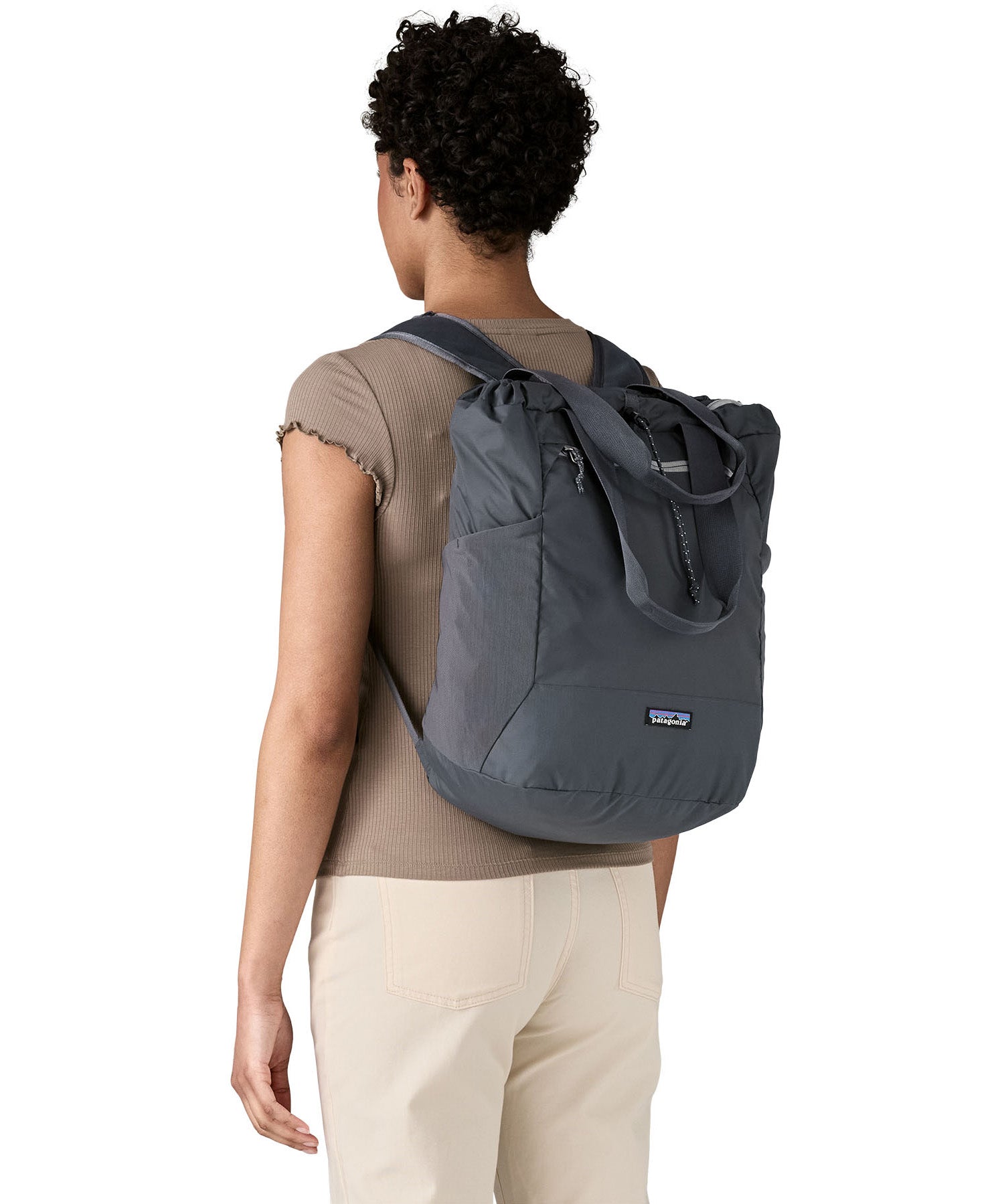 Patagonia Terravia tote bag in smolder blue worn by a adult on the back showing the carrying handle details and side mesh pockets for holding bottles