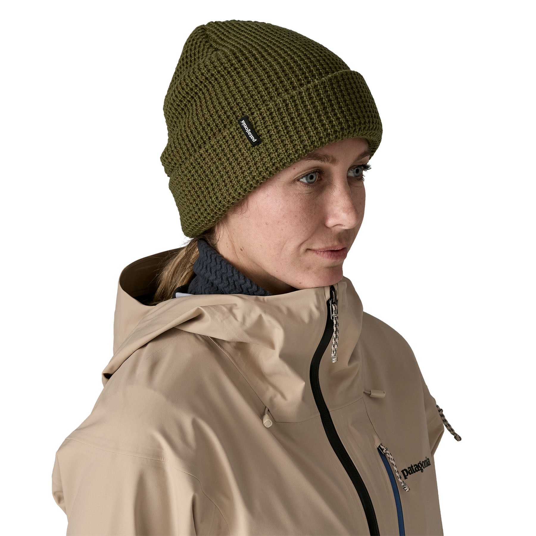A woman wearing the Patagonia snowdrifter beanie in tent green with rolled up brim. Features a brand logo patch stitched on the side available at Babipur.