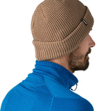 Side and back view of the Patagonia adult snow drifter beanie in a pale khaki colour. showing the brim turned up and the logo branding on the side