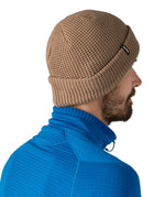 Side and back view of the Patagonia adult snow drifter beanie in a pale khaki colour. showing the brim turned up and the logo branding on the side