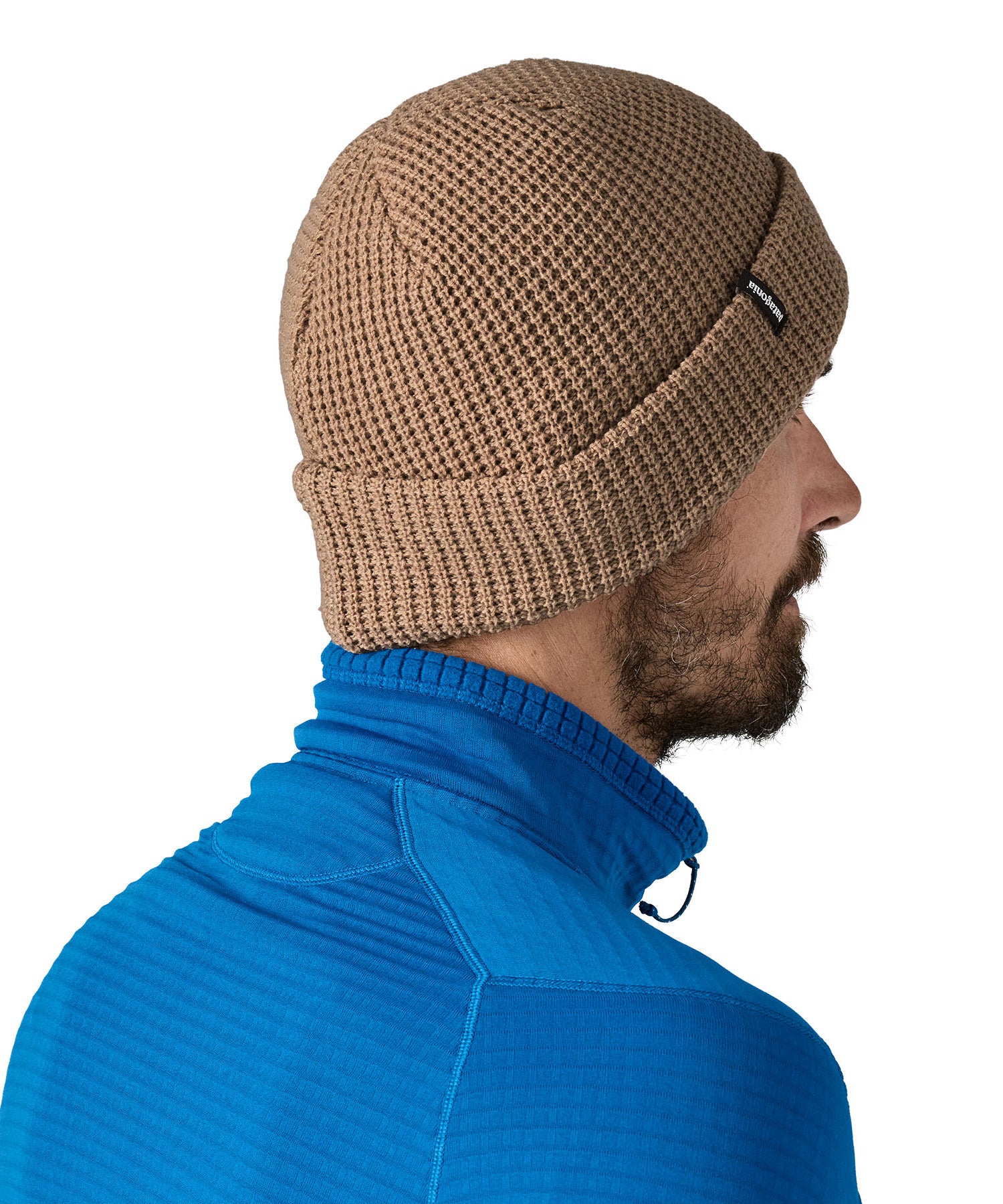 Side and back view of the Patagonia adult snow drifter beanie in a pale khaki colour. showing the brim turned up and the logo branding on the side