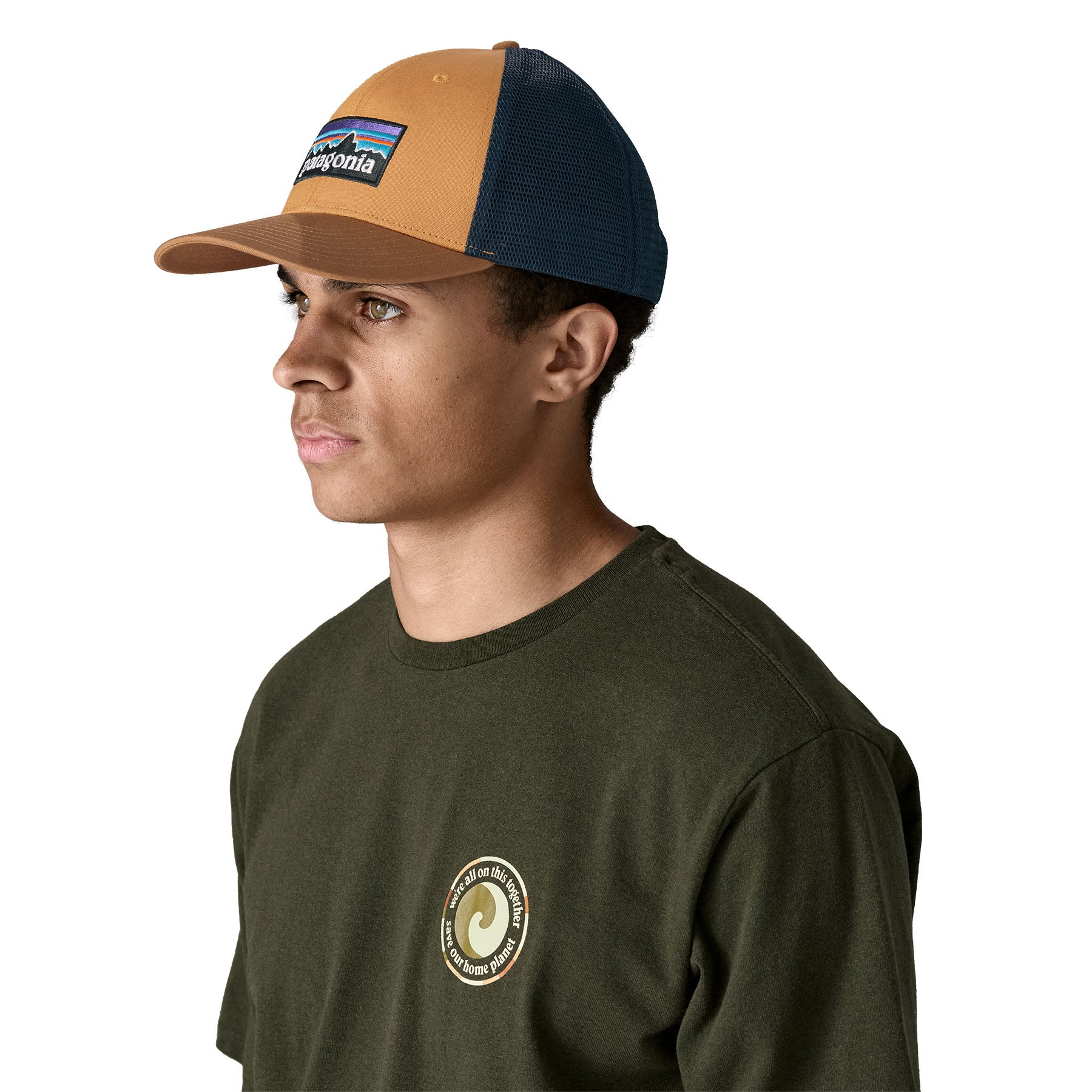 A man wearing the Patagonia adult talon gold hat. A trucker style cap with a low profile in gold colour and features a navy mesh back with a logo embroidery on the front panel available at Babipur.