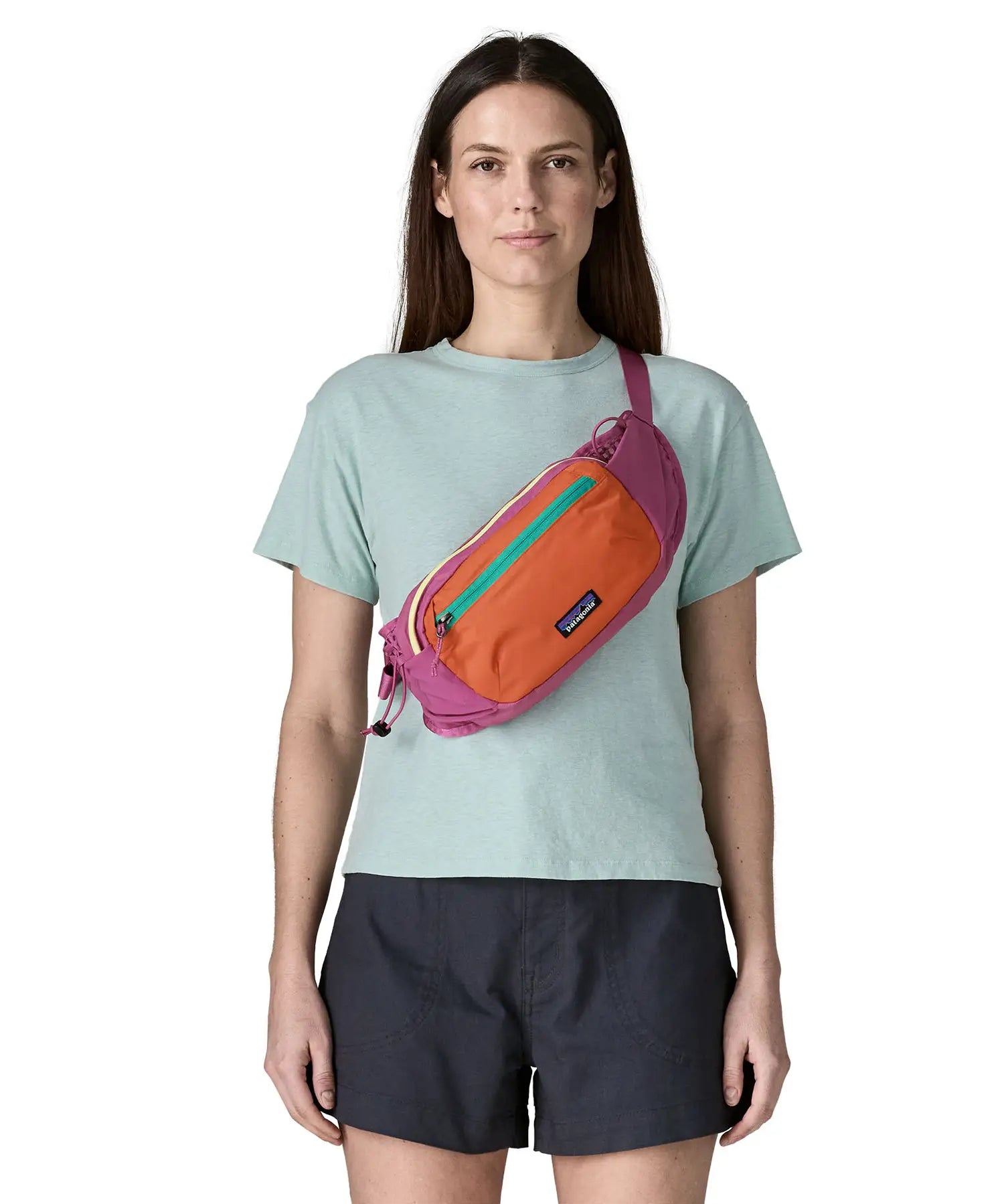 Woman wearing Patagonia's terravia hip pack in bright purple with an orange front panel over the shoulder