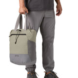 A close up of the Patagonia Terravia tote bag in river rock green carried by an adult by the handles showing the front zip details and 2 side pockets.