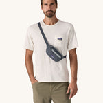 A man wearing the Patagonia Terravia Mini Bum Bag Hip Pack in a Smolder Blue colour on his shoulder across his chest. 