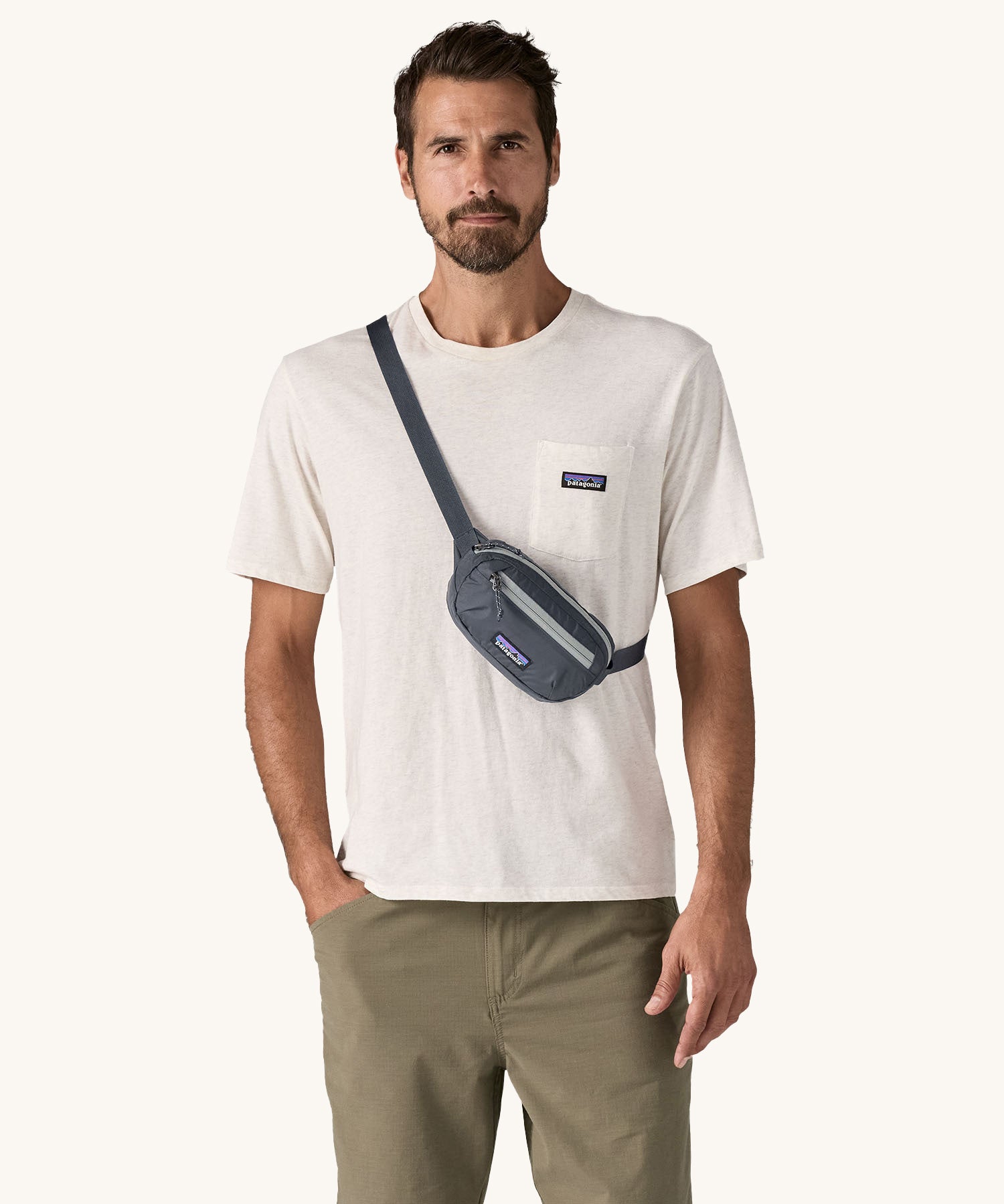 A man wearing the Patagonia Terravia Mini Bum Bag Hip Pack in a Smolder Blue colour on his shoulder across his chest. 
