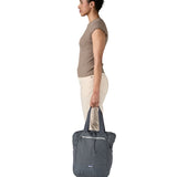 A side view of the Patagonia Terravia tote bag in smolder blue carried by an adult by the handles showing the front zip details and 2 side pockets.