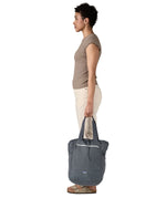 A side view of the Patagonia Terravia tote bag in smolder blue carried by an adult by the handles showing the front zip details and 2 side pockets.