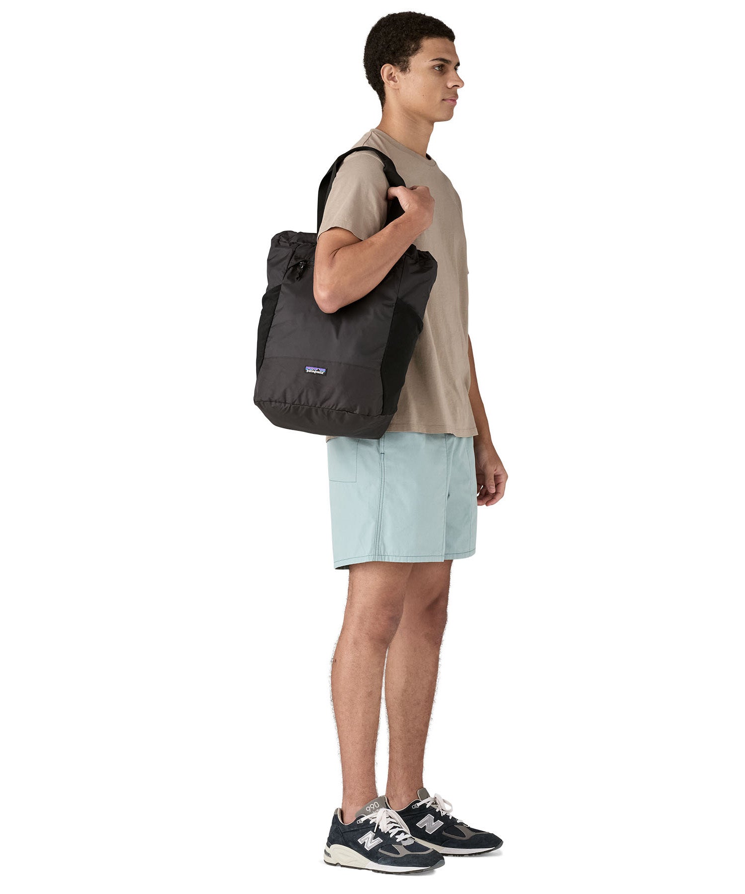 Patagonia Terravia tote bag in black carried by a adult on the shoulder showing the side pockets for holding bottles