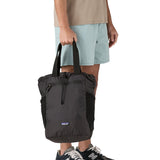 A close up of the Patagonia Terravia tote bag in black carried by an adult by the handles showing the front zip details and 2 side pockets.
