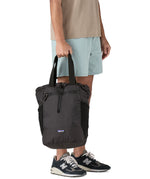 A close up of the Patagonia Terravia tote bag in black carried by an adult by the handles showing the front zip details and 2 side pockets.