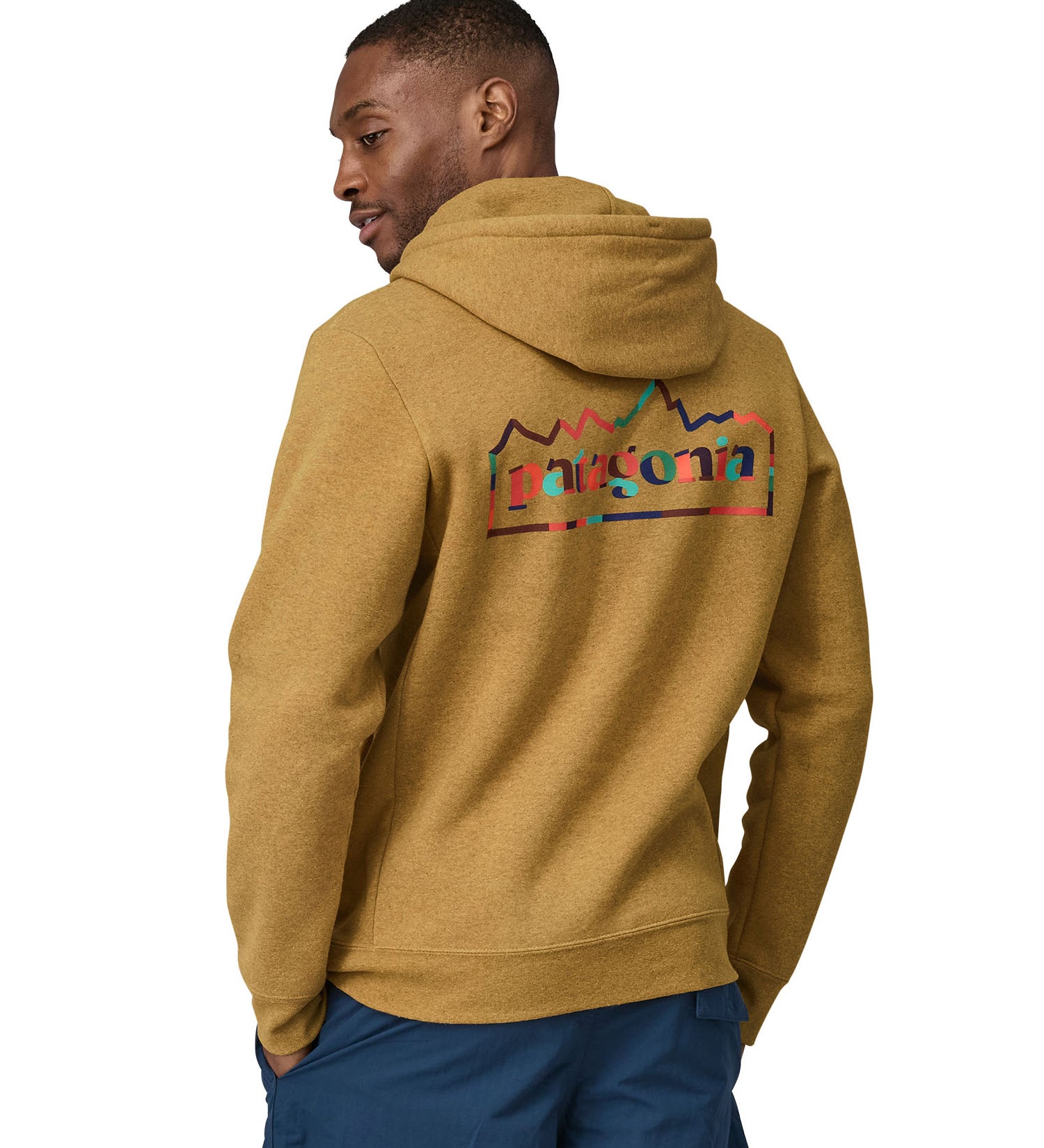 A man wearing a Patagonia Unity Fitz Uprisal Hoody in a yellow colour stood in front of a plain background. The man is facing away from the camera, showing the back of the top. 