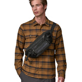 A man wearing the patagonia waist pack in black over the shoulder. A 100% recycled material pack with 2 main compartments and adjustable shoulder strap.