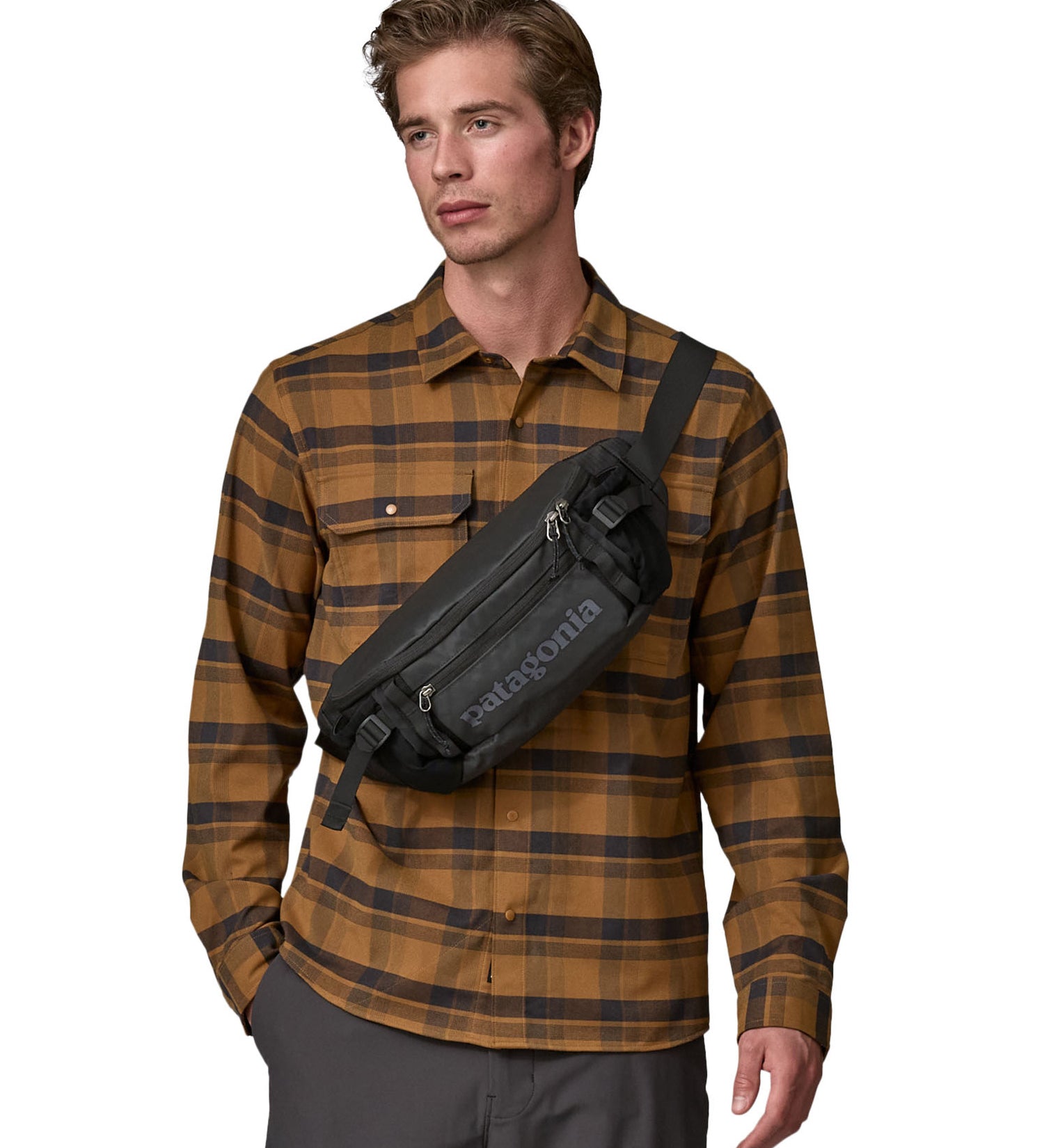 A man wearing the patagonia waist pack in black over the shoulder. A 100% recycled material pack with 2 main compartments and adjustable shoulder strap.