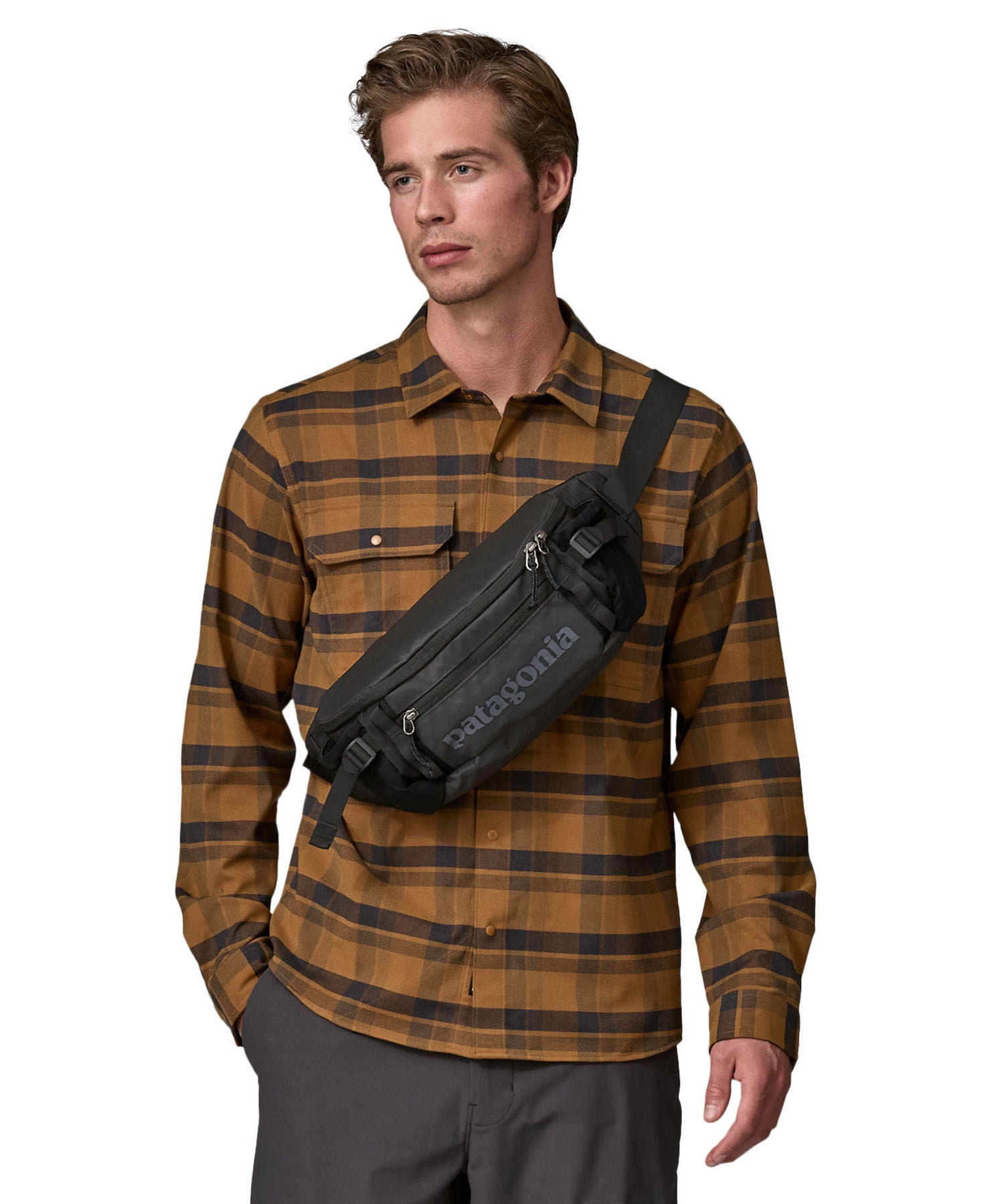 A man wearing the patagonia waist pack in black over the shoulder. A 100% recycled material pack with 2 main compartments and adjustable shoulder strap.